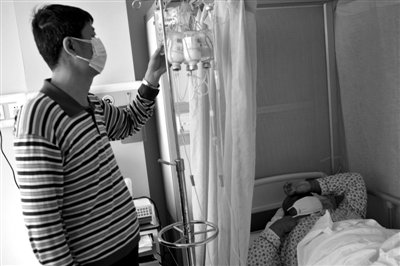 王国祥在查看吊瓶。因为体重原因，患有白血病的儿子治疗费高出常人一倍，王国祥一家陷入“无钱治病”的窘境。